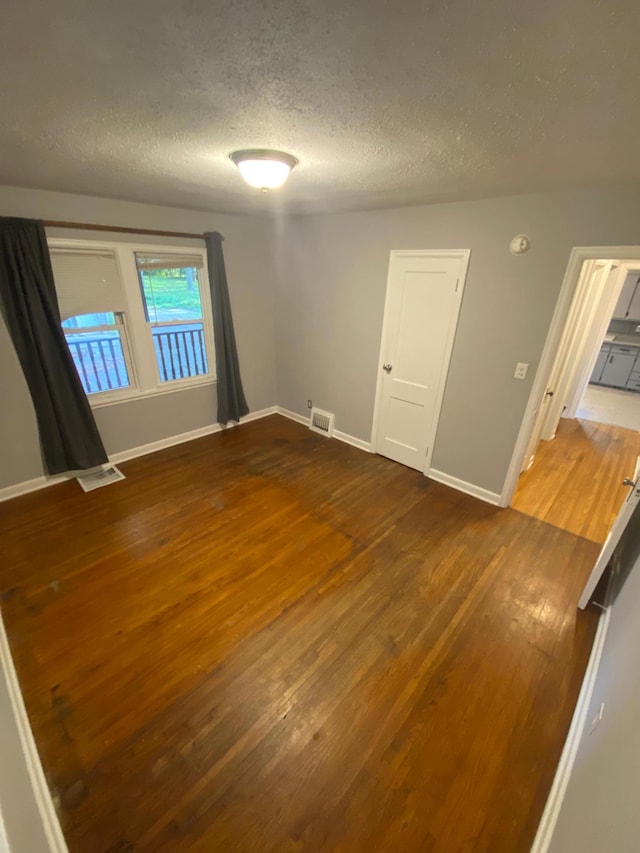 spare room featuring a textured ceiling, wood finished floors, visible vents, and baseboards