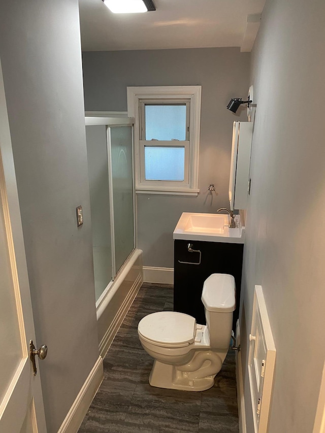 bathroom with toilet, wood finished floors, baseboards, enclosed tub / shower combo, and vanity