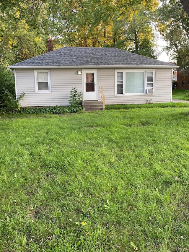 single story home featuring entry steps, a chimney, a front lawn, and a shingled roof