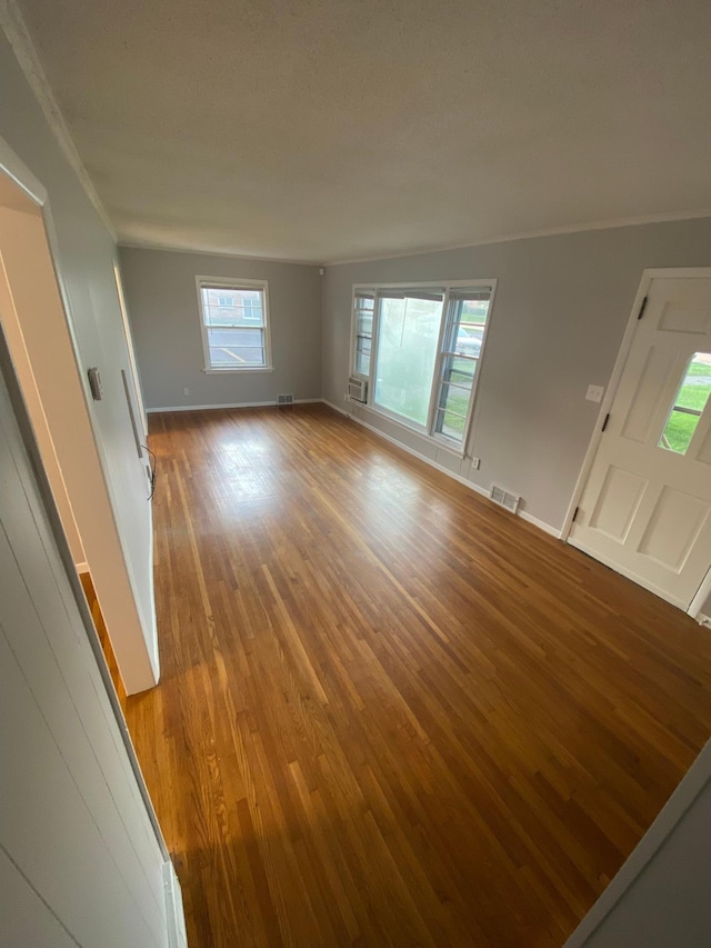 unfurnished living room with visible vents, baseboards, wood finished floors, and ornamental molding