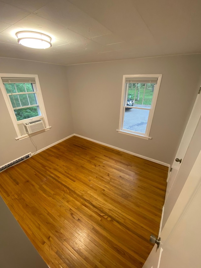 unfurnished room featuring baseboard heating, a healthy amount of sunlight, baseboards, and wood-type flooring