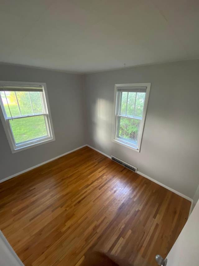 spare room with wood finished floors, visible vents, a wealth of natural light, and baseboards