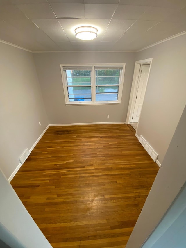 empty room featuring baseboards, wood finished floors, visible vents, and ornamental molding