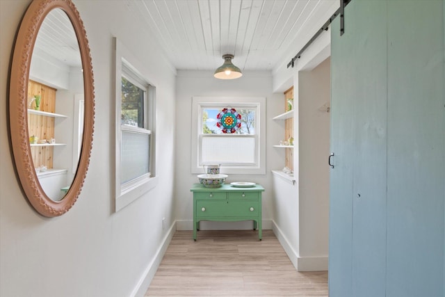 hall with a barn door, light wood-style flooring, wood ceiling, and baseboards