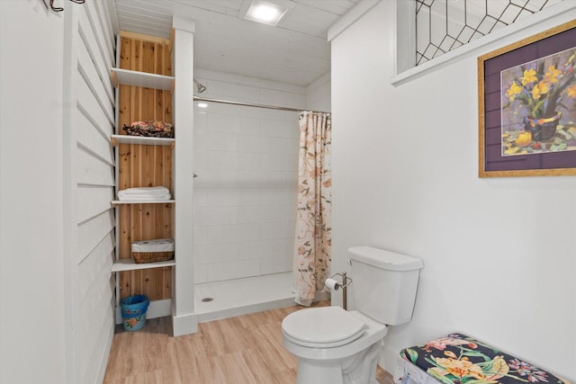 bathroom with tiled shower, toilet, and wood finished floors