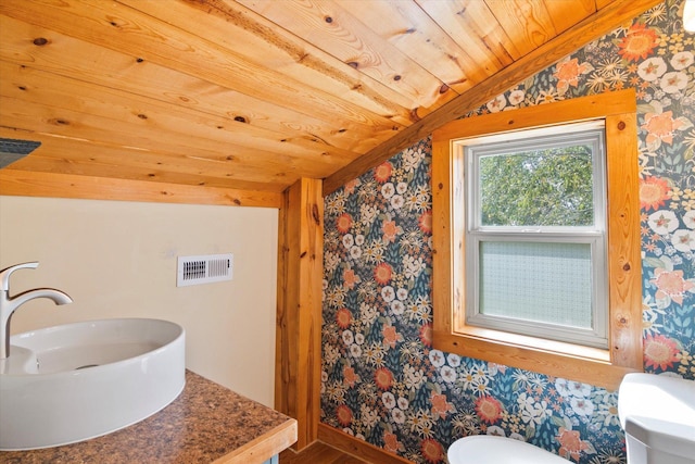 bathroom featuring wallpapered walls, wooden ceiling, toilet, and a sink