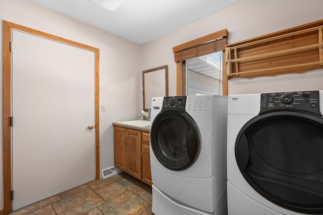 laundry room with visible vents, cabinet space, a sink, stone tile flooring, and washer and clothes dryer