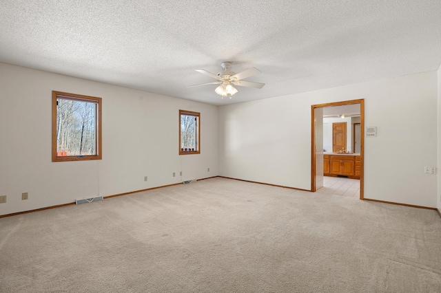 empty room with light carpet, visible vents, a textured ceiling, and ceiling fan