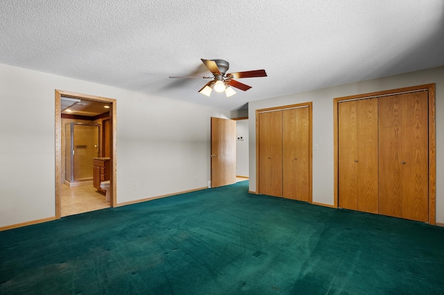 unfurnished bedroom with baseboards, carpet floors, multiple closets, a textured ceiling, and connected bathroom