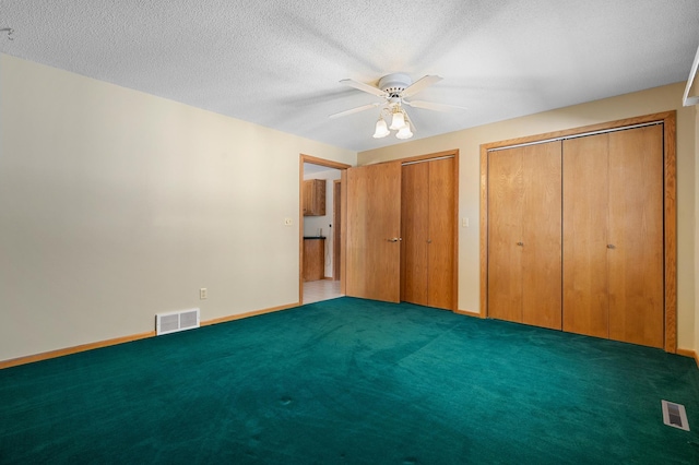 unfurnished bedroom featuring visible vents, multiple closets, carpet, and a textured ceiling