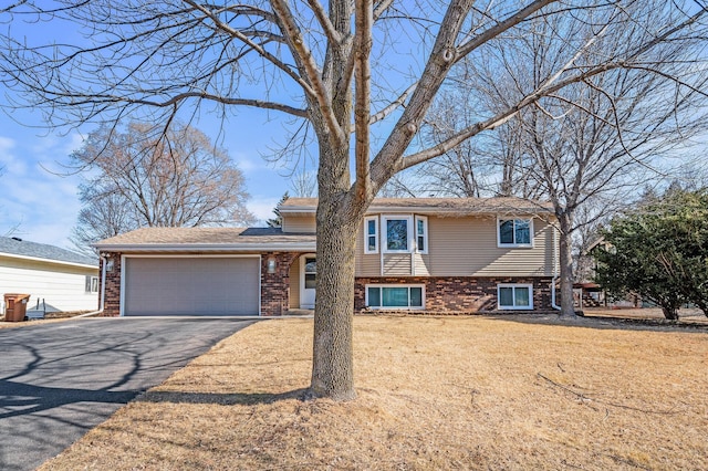 tri-level home with a front yard, brick siding, a garage, and driveway