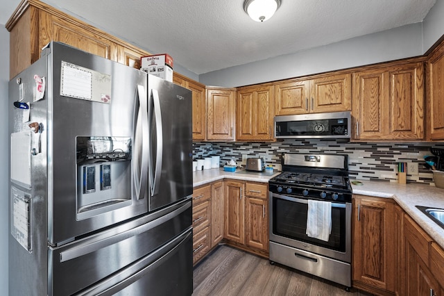 kitchen with dark wood-type flooring, appliances with stainless steel finishes, brown cabinetry, light countertops, and decorative backsplash