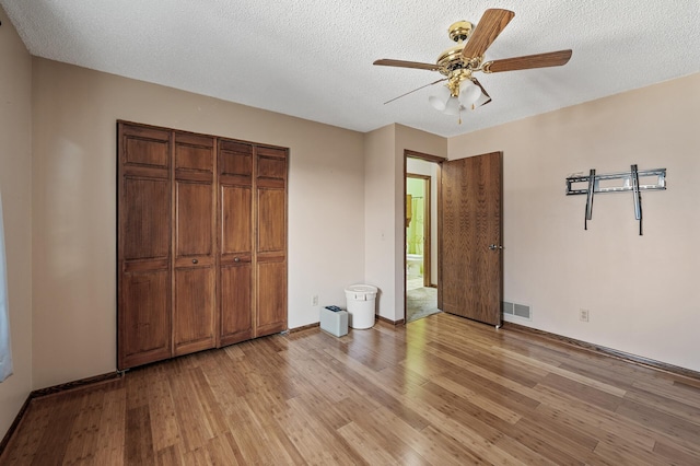 unfurnished bedroom featuring light wood finished floors, visible vents, a closet, a textured ceiling, and a ceiling fan