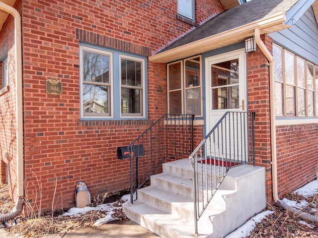 entrance to property featuring brick siding and roof with shingles