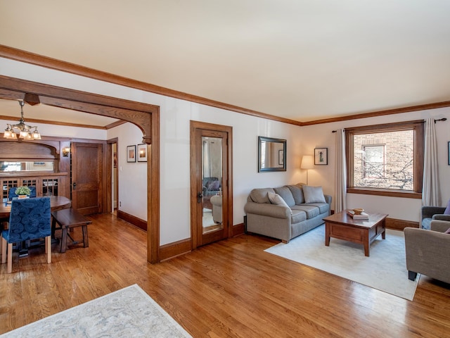 living room featuring light wood-style flooring, baseboards, an inviting chandelier, and ornamental molding