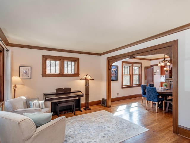 living room featuring baseboards, light wood-style floors, a healthy amount of sunlight, and ornamental molding