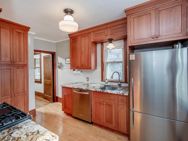 kitchen with brown cabinetry, light wood finished floors, a sink, appliances with stainless steel finishes, and crown molding