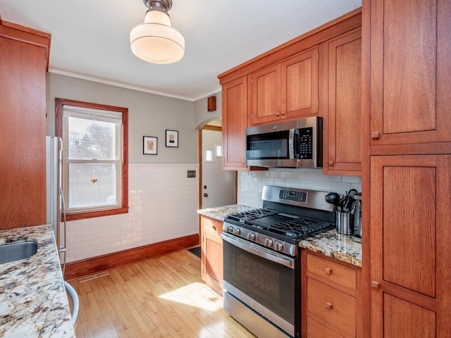 kitchen featuring crown molding, light wood-type flooring, light stone counters, brown cabinetry, and stainless steel appliances