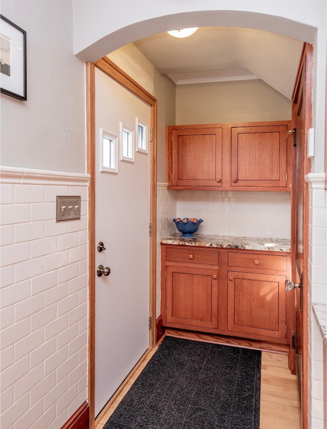 kitchen featuring a wainscoted wall, arched walkways, tile walls, and brown cabinetry