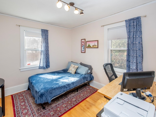 bedroom with multiple windows, baseboards, and wood finished floors