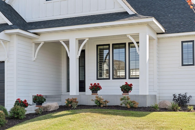 doorway to property featuring board and batten siding, a lawn, and roof with shingles