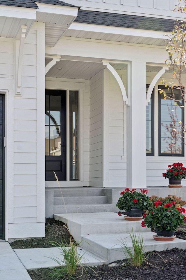 entrance to property with covered porch and a shingled roof