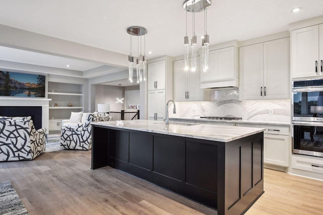 kitchen with light wood-style flooring, a sink, light stone counters, white cabinetry, and appliances with stainless steel finishes