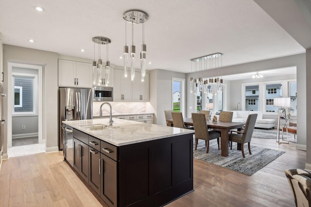 kitchen featuring a sink, stainless steel microwave, white cabinetry, light wood-style floors, and light stone countertops