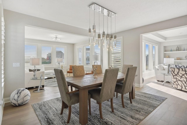 dining room featuring a notable chandelier, baseboards, light wood-type flooring, and built in features