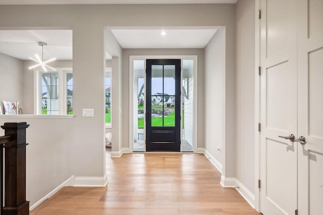 foyer entrance featuring an inviting chandelier, light wood-style flooring, and baseboards