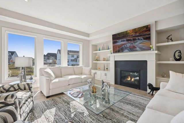 living room featuring a glass covered fireplace, built in shelves, and wood finished floors