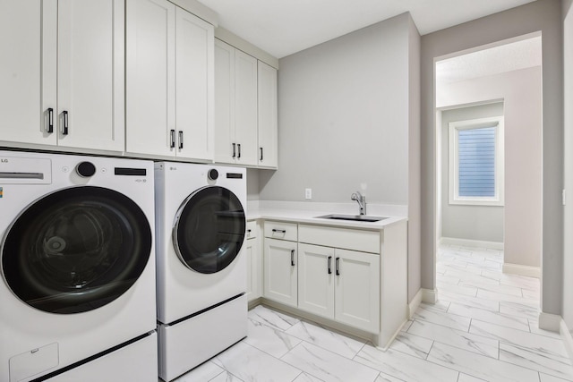 clothes washing area featuring marble finish floor, a sink, washer and dryer, cabinet space, and baseboards