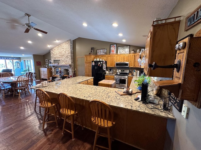 kitchen with lofted ceiling, brown cabinets, appliances with stainless steel finishes, a peninsula, and dark wood-style floors