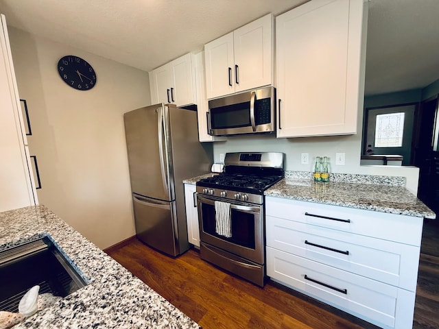 kitchen featuring dark wood-style floors, appliances with stainless steel finishes, white cabinetry, and light stone countertops