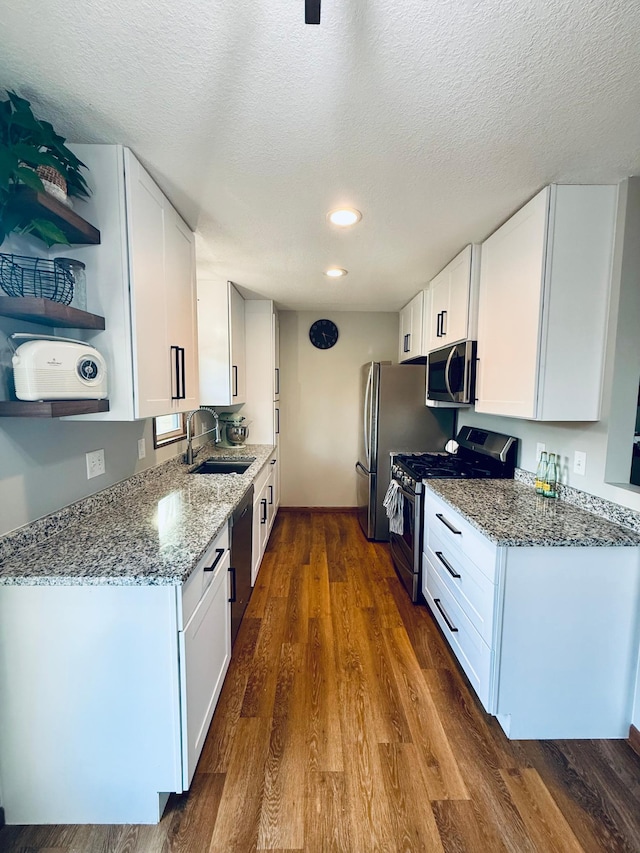 kitchen with dark wood-type flooring, light stone counters, stainless steel appliances, white cabinetry, and a sink