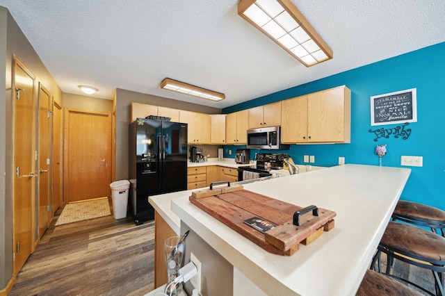 kitchen featuring light brown cabinets, light countertops, a kitchen breakfast bar, a peninsula, and black appliances