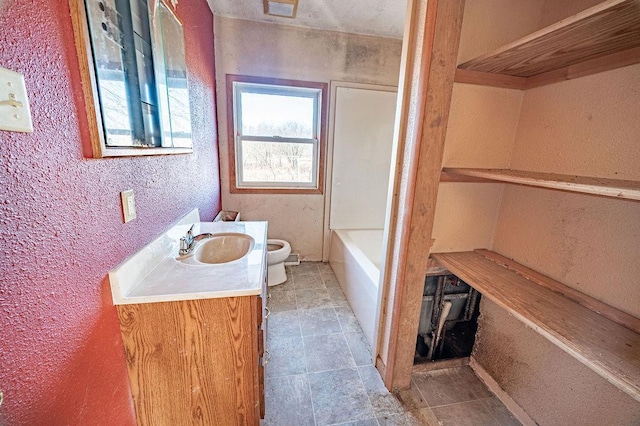 bathroom featuring a tub, toilet, vanity, and a textured wall