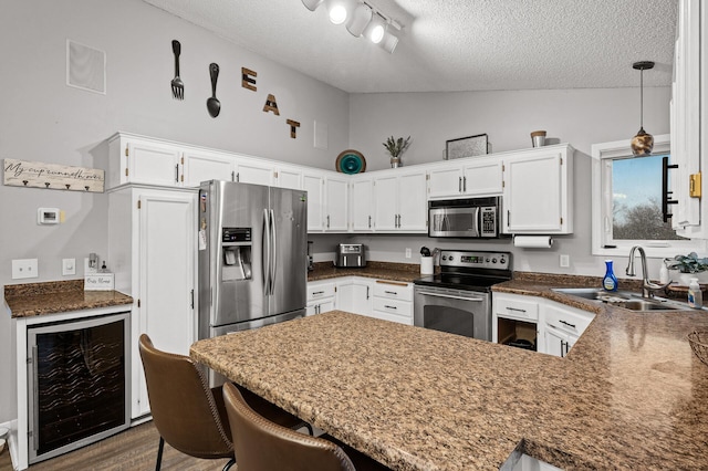 kitchen with beverage cooler, vaulted ceiling, appliances with stainless steel finishes, a peninsula, and a sink