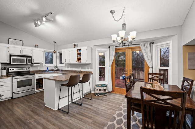 kitchen featuring dark countertops, vaulted ceiling, a peninsula, stainless steel appliances, and dark wood-style flooring