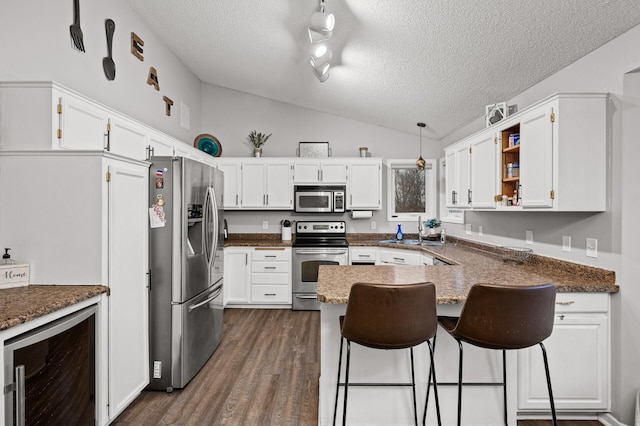 kitchen with dark wood finished floors, wine cooler, appliances with stainless steel finishes, a peninsula, and lofted ceiling