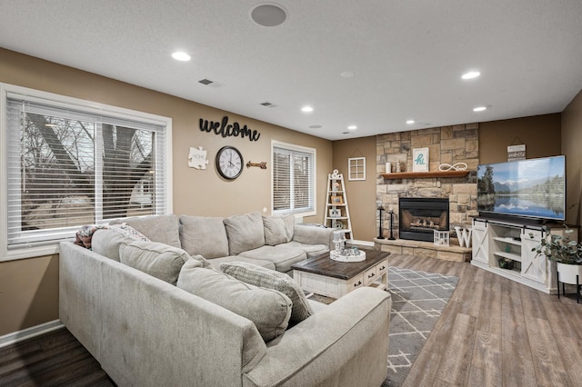 living room featuring recessed lighting, visible vents, a stone fireplace, and wood finished floors