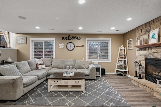 living area with a stone fireplace, wood finished floors, visible vents, and a textured ceiling