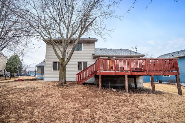 back of house with stairway, a trampoline, roof with shingles, and a deck