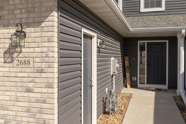 view of exterior entry with roof with shingles