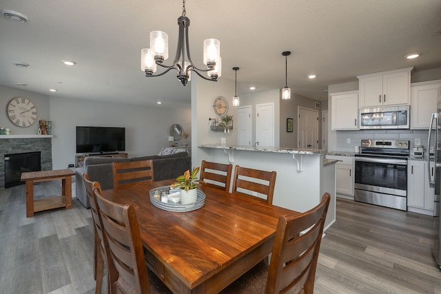 dining area featuring recessed lighting, a stone fireplace, wood finished floors, and an inviting chandelier