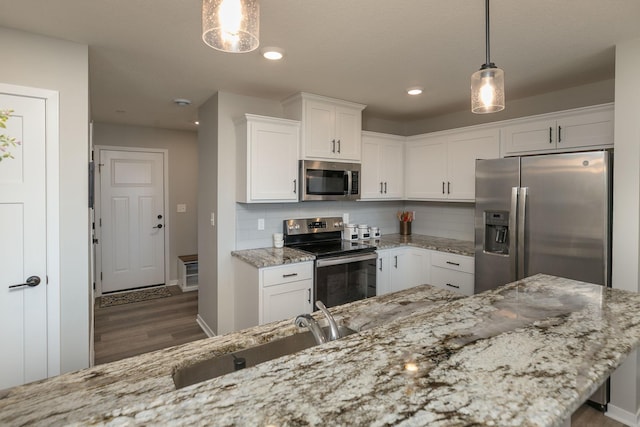 kitchen with a sink, light stone counters, backsplash, white cabinetry, and appliances with stainless steel finishes