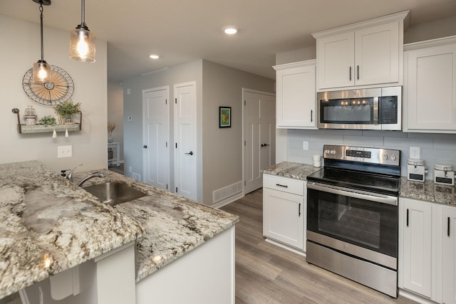 kitchen with tasteful backsplash, light stone countertops, appliances with stainless steel finishes, light wood-style floors, and a sink