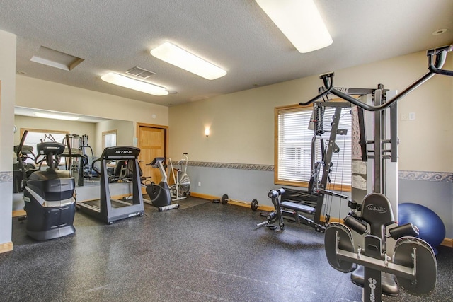 workout area featuring baseboards, visible vents, and a textured ceiling