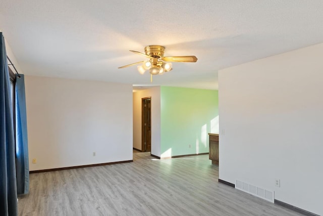 spare room featuring light wood-type flooring, visible vents, a textured ceiling, baseboards, and ceiling fan