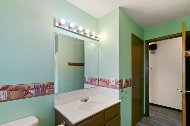 half bathroom featuring toilet, wood finished floors, vanity, and a textured ceiling